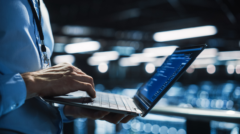 Man holding a laptop from waist down, blue background